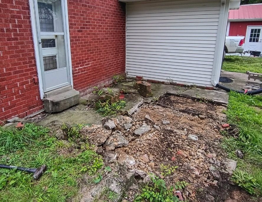 Old concrete patio broken out and removed down to base beside a brick house